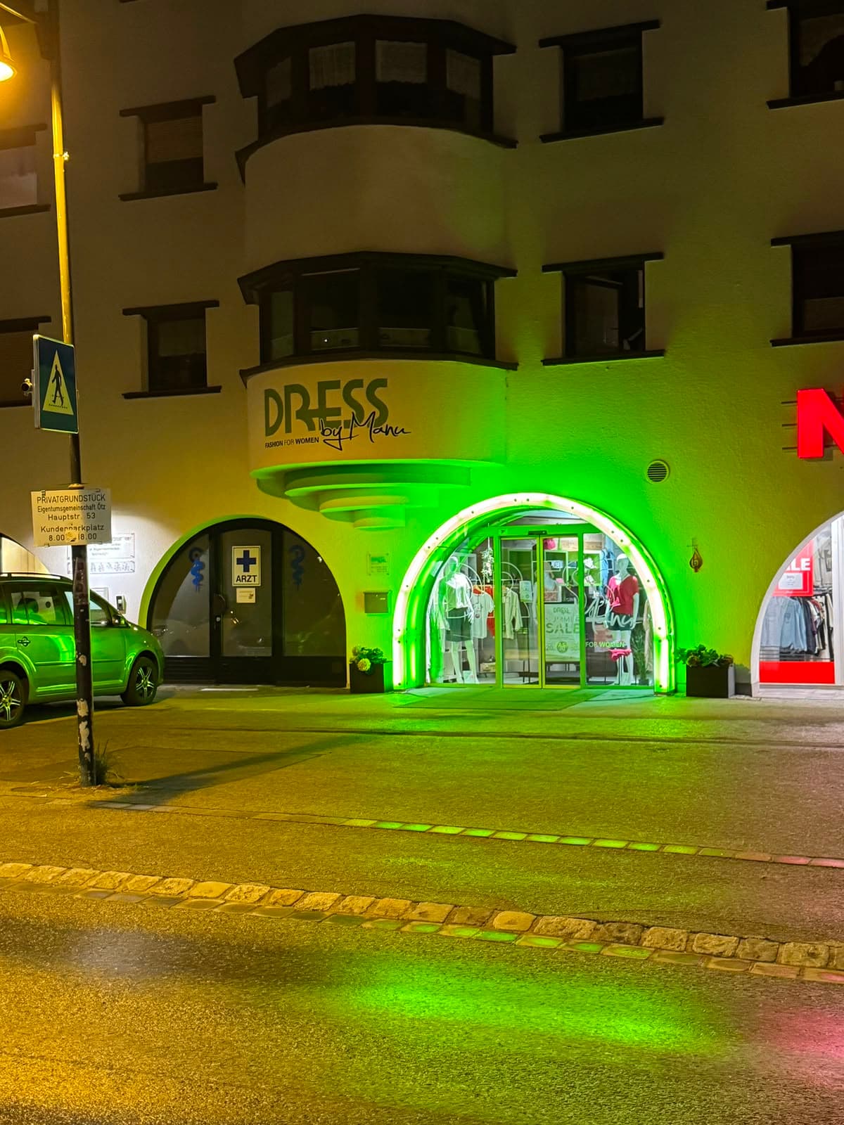 Nächtliche Außenansicht von DRESS by Manu in Oetz mit grün beleuchtetem Eingang